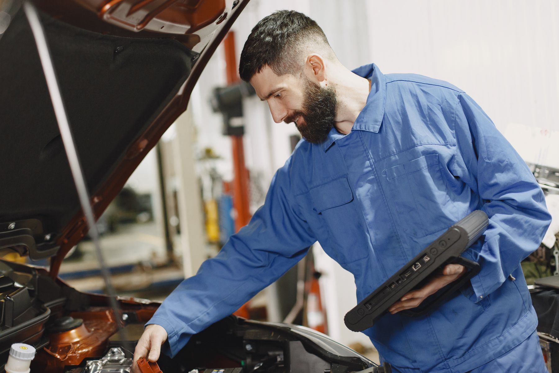 Mécanicien en bleu de travail penché sur un moteur, capot ouvert